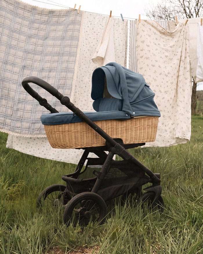 AngelCab pram with a blue hood and rattan basket on the grass beside a washing line